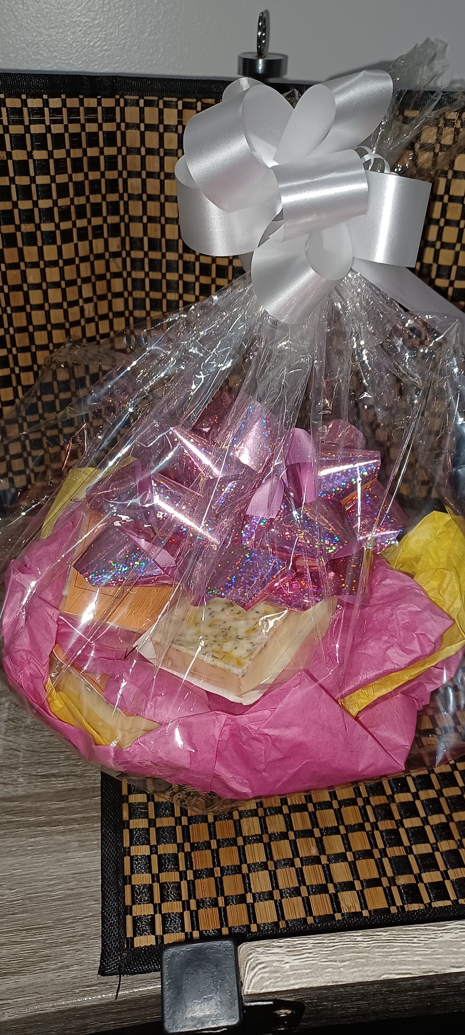 An APSTERGO gift wrapped in clear cellophane with pink tissue and a big white bow for Mother’s Day, holding a mix of different scented bars